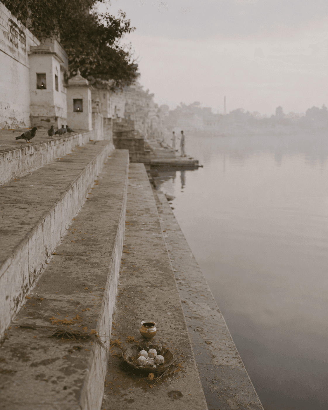 Ghat steps at Pushkar lake at dawn during Pitru Paksha, pind offerings and a brass lota on the lowest step